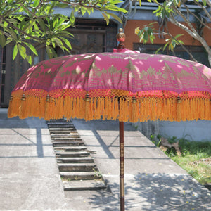 Balinese pink parasol with gold decorative patterns and yellow fringe outdoors