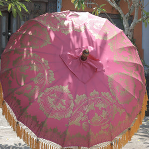 Balinese pink parasol with gold floral patterns and tassel fringe, outdoor setting