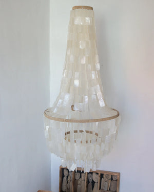 Handmade seashell chandelier with layered white shell pieces hanging in a minimalist room