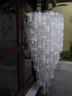 Handmade cascading seashell chandelier with round white shells by glass doors outdoors