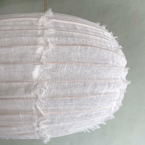 Close-up of a round, white fabric pendant light with textured, fringed edges