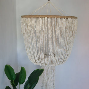 Handmade seashell chandelier with cascading strands, boho coastal decor, plant nearby