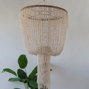 Handmade Balinese seashell chandelier with cascading beads, hanging above indoor plant