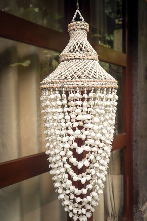 Handmade Balinese seashell chandelier with intricate beading, hanging by a window