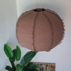 Brown fabric pendant lamp with fringe details hanging above green indoor plant in modern decor