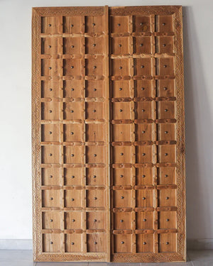 Hand-carved Balinese wooden double doors with geometric panels and decorative border.