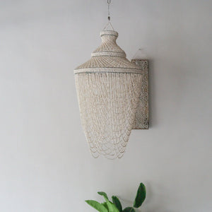 Handmade Balinese seashell chandelier on beige wall above green indoor plant