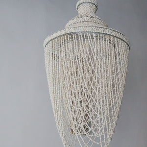 Handmade Balinese seashell chandelier with cascading beads against a plain wall