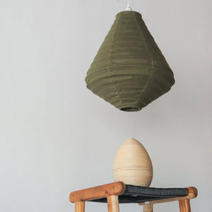 Olive green pendant lamp and wooden decor egg on rustic chair against neutral wall