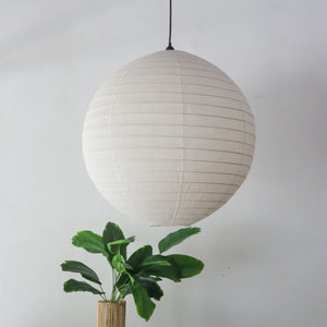 Linen lantern chandelier in off-white, round shape, hanging elegantly above a green plant.
