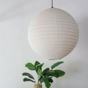 Off white round linen lantern chandelier hanging above a green plant, handcrafted in Bali.