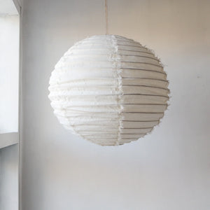 Handmade round fabric pendant lamp with textured white surface, hanging in a minimalist room