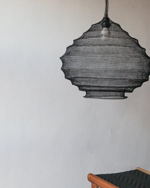 Handcrafted black rattan pendant light hanging above wooden chair in minimalist room