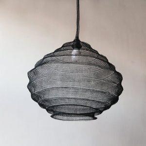 Black wire mesh pendant lamp with sculptural, handcrafted design against a neutral wall