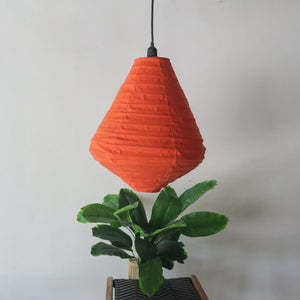 Handmade orange pendant lamp with geometric shade above green indoor plant