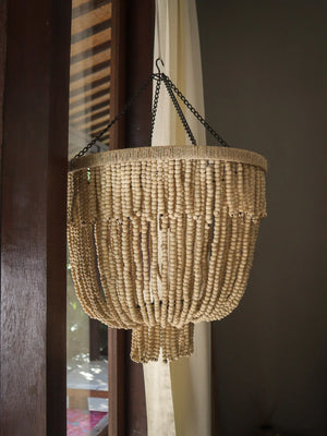 Handmade Balinese beaded chandelier with natural wood beads hanging by a window indoors