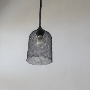 Handcrafted black wire mesh pendant light with exposed bulb against plain wall