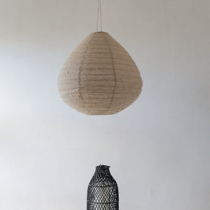 Handmade natural fiber pendant lamp and woven black vase against a minimalist white wall