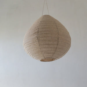 Handcrafted beige fabric pendant light with natural texture against a neutral wall.