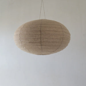Handmade natural fiber pendant light with a neutral textured finish, hanging against a plain wall.