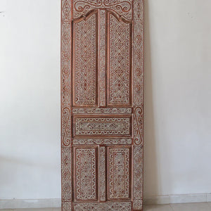 Hand-carved Balinese wooden door with intricate traditional patterns, set against a white wall.