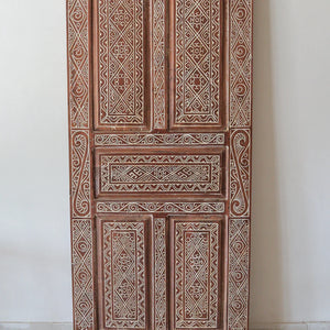 Hand-carved Balinese wooden door with intricate geometric patterns in white detailing