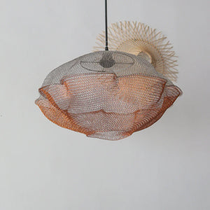 Handmade rattan and wire pendant lamp with wavy design hanging against a white wall