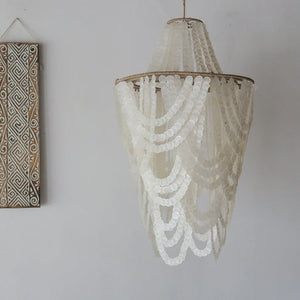 Handmade Balinese seashell chandelier with cascading white capiz shells beside a carved wall art.