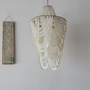 Elegant hanging seashell chandelier with hand-carved wooden wall decor on white wall