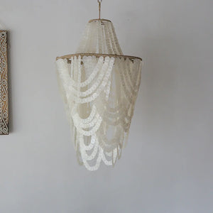Handmade seashell chandelier with cascading white shell strands against a plain wall.
