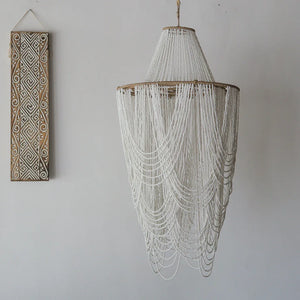 Balinese white seashell beaded chandelier with hand-carved wood wall art on white wall