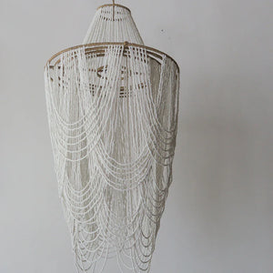 Handmade Balinese seashell chandelier with white beaded strands against plain wall