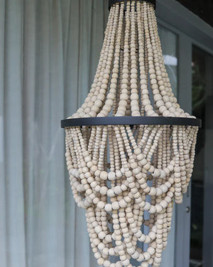 Handmade wooden bead chandelier with cascading strands in front of sheer curtains