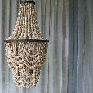 Handmade wooden bead chandelier pendant in front of sheer curtains.