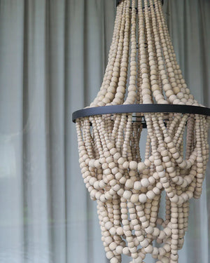 Handmade wooden beaded chandelier with natural finish in front of sheer curtains