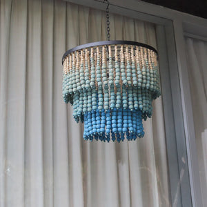 Handmade blue beaded chandelier with tiered strands, hanging indoors by a window