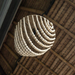 Handmade beaded chandelier with natural wood beads hanging from a thatched ceiling.