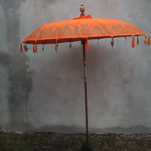 Handmade Balinese orange parasol with carved pole and decorative hanging tassels outdoors