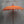 Balinese orange hand-carved parasol with tassels and ornate wooden pole against grey wall