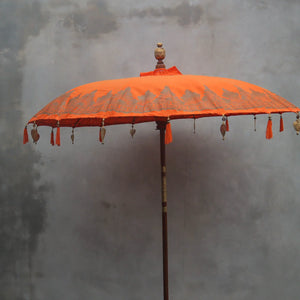 Balinese orange hand-carved parasol with tassels and ornate wooden pole against grey wall