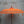Balinese orange decorative umbrella with tassels and carved wooden pole against gray wall