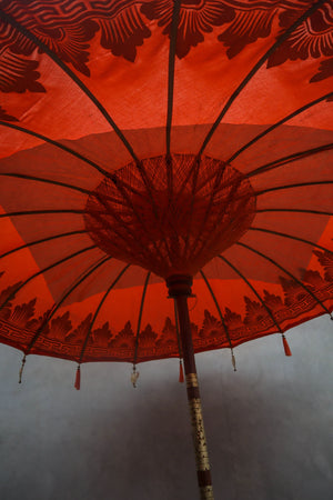 Traditional Balinese red parasol with intricate patterns and wooden pole