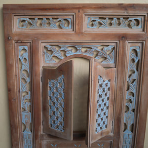 Hand-carved Balinese teak wood window with intricate floral patterns and blue accents