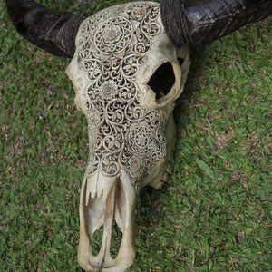 Hand-carved buffalo skull with intricate Balinese patterns on grass background