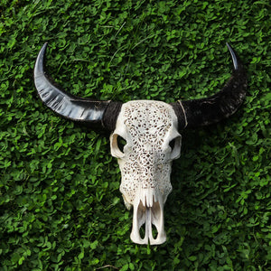 Hand-carved decorative buffalo skull with intricate Balinese patterns on green foliage background