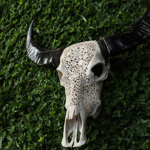 Hand-carved Balinese bull skull with intricate patterns mounted on a green leafy wall