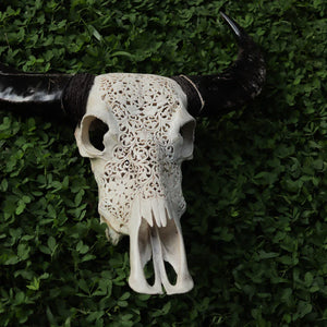Intricately hand-carved Balinese buffalo skull wall decor on green foliage background