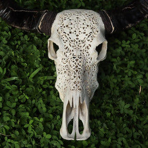 Hand-carved Balinese buffalo skull with intricate floral patterns on green foliage