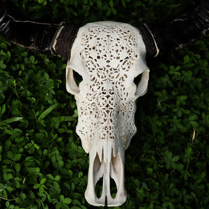 Hand-carved Balinese cow skull with intricate floral patterns on green foliage