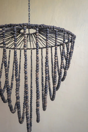 Handmade Balinese wooden bead chandelier with natural dark finish, hanging on beige wall